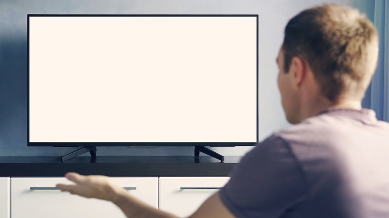 A man looking at a blank TV screen and making a frustrated gesture