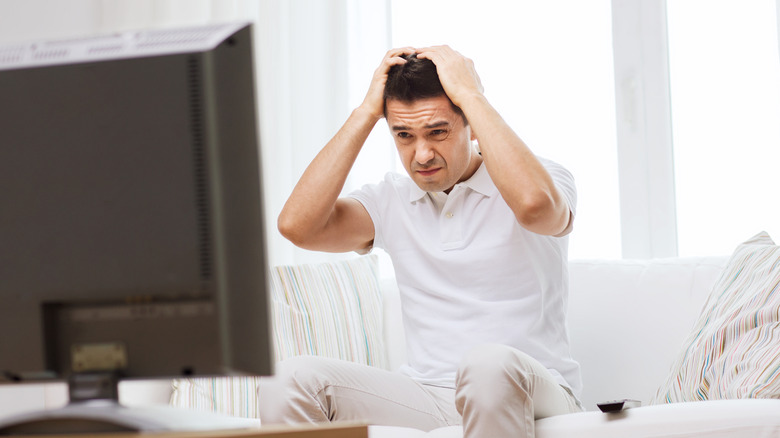 A disappointed man looking at a TV screen