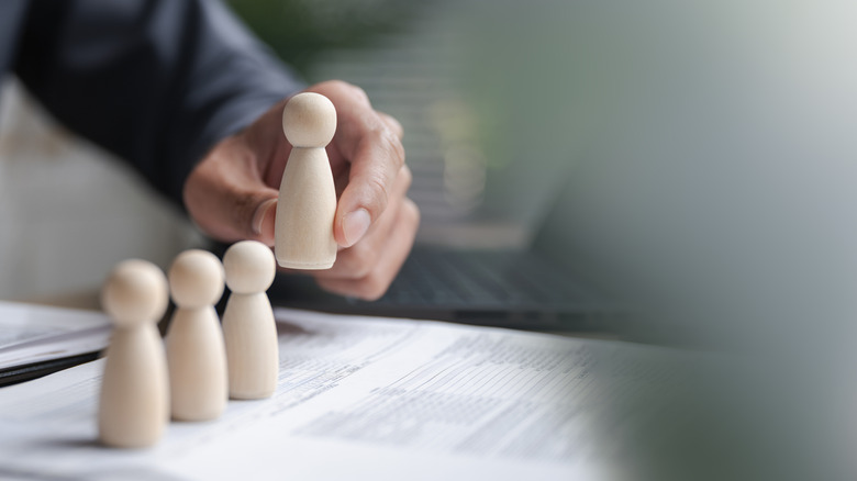 A hand picking up a wooden figure in front of three others on a desk.