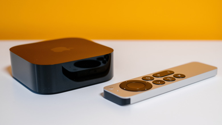 Apple TV 4K sitting on white table next to remote, with orange background