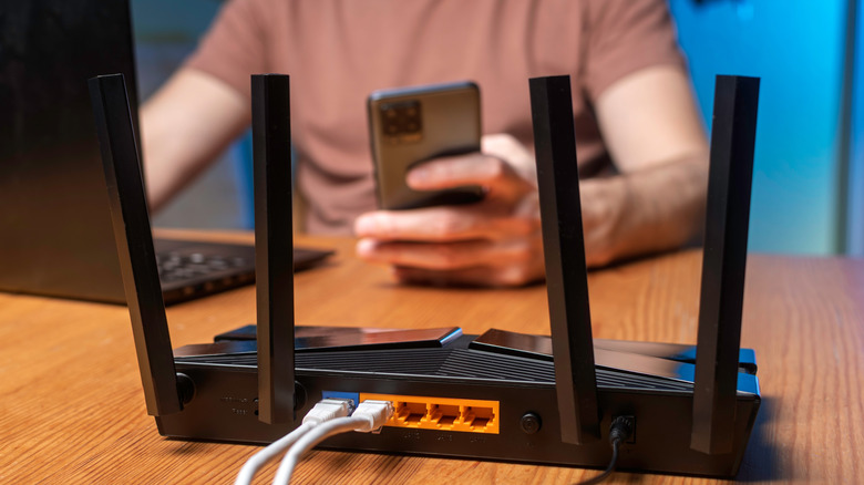 A picture of a router on a desk with a man on his phone in the background