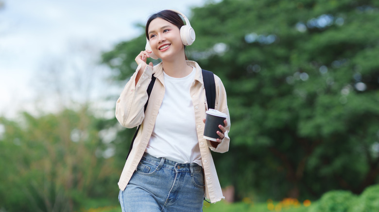 A lady wearing headphones while walking through an outdoor park