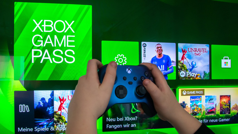 A person holding up a blue Xbox controller against a splash screen of the Xbox home page