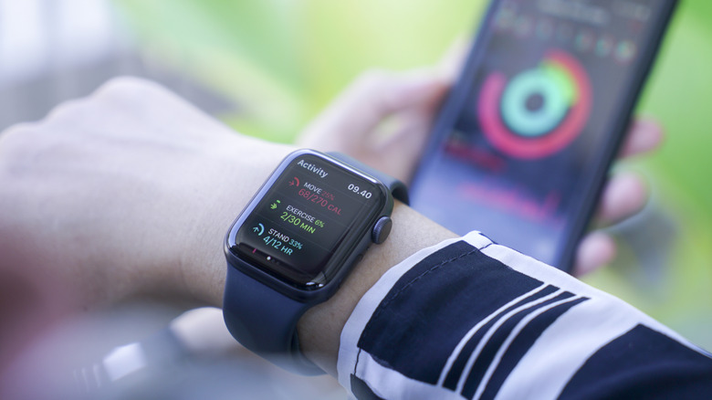 A wrist with an Apple Watch, a faded out iPhone in the background showing the app.