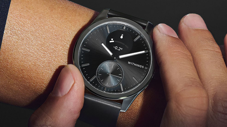 A close-up of the Withings ScanWatch two on a wrist, fingers touching the buttons.