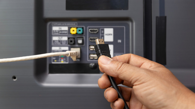 A person plugging in an HDMI cable to a back of a TV