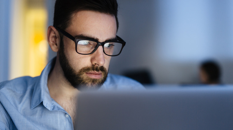 A man that wears glasses looking at a computer screen