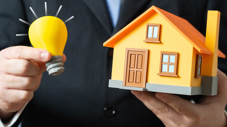 Man holding light bulb graphic next to model of private home