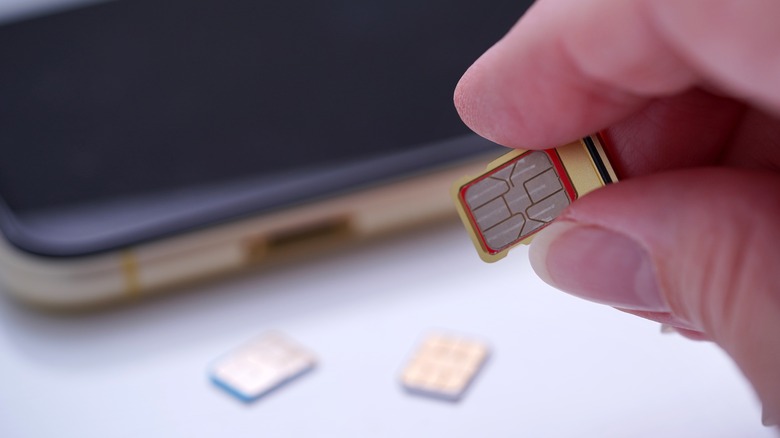 A finger and thumb holding a SIM card with a smart phone and two additional SIM cards in the background