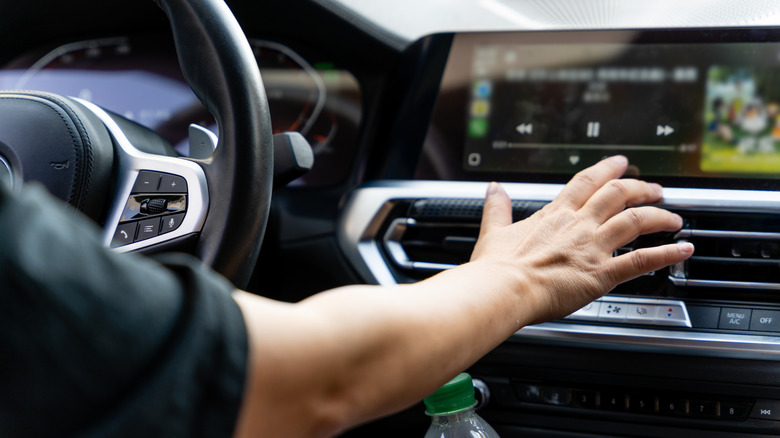 Close up of a driver's hand reaching for the touchscreen on the car's dashboard