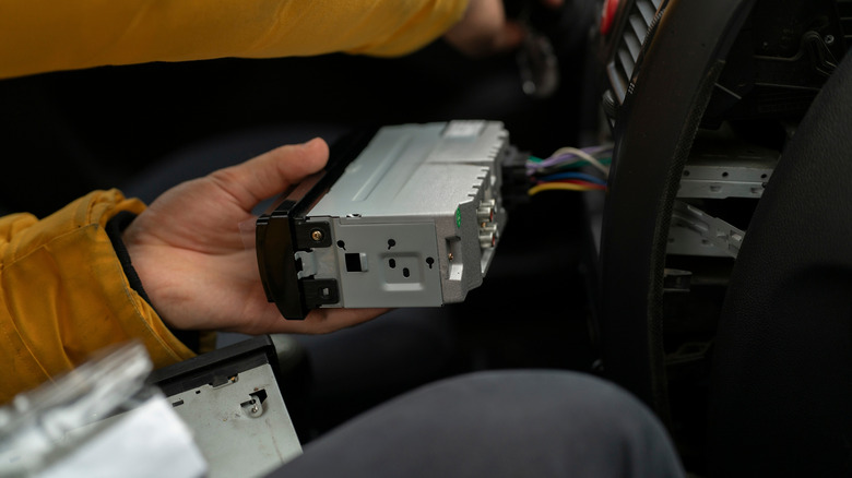 A hand installing a new stereo system from the driver's seat of the car.