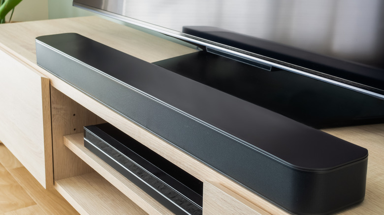 A black soundbar placed on a TV unit below a TV screen