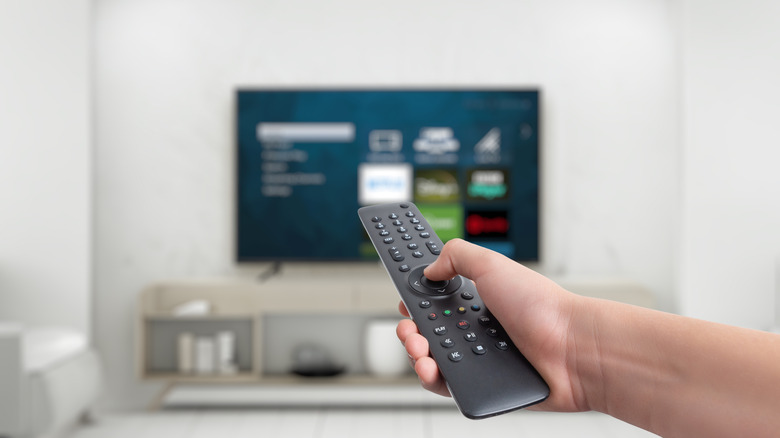 A hand holding a TV remote pointed at a TV