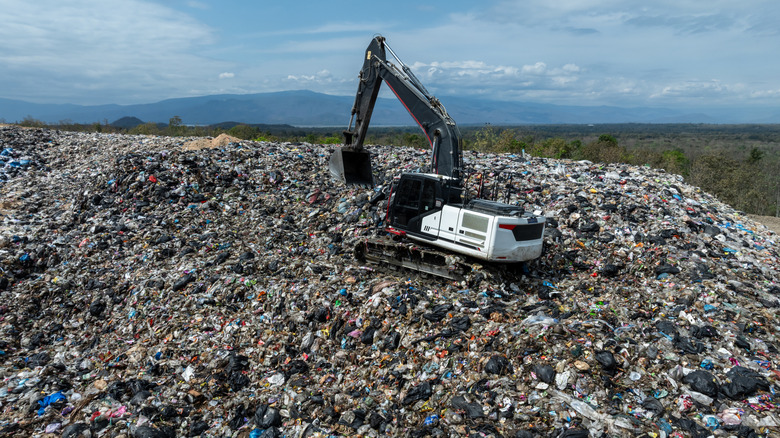 Heavy machinery moving up a landfill with garbage visible.