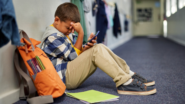 a sad boy sitting in a school hall and looking at his phone