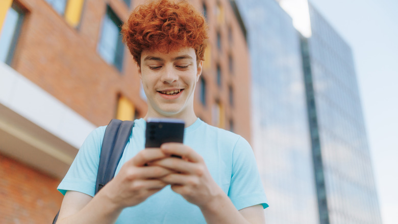 a teenage boy smiling and looking at his smartphone
