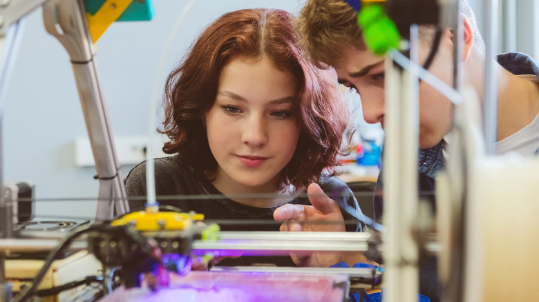 Two people observing a 3D printer in action.