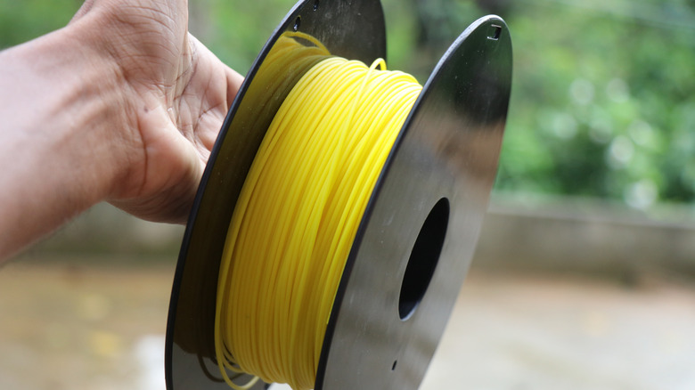 Hand holding a spool of yellow 3D printer filament.