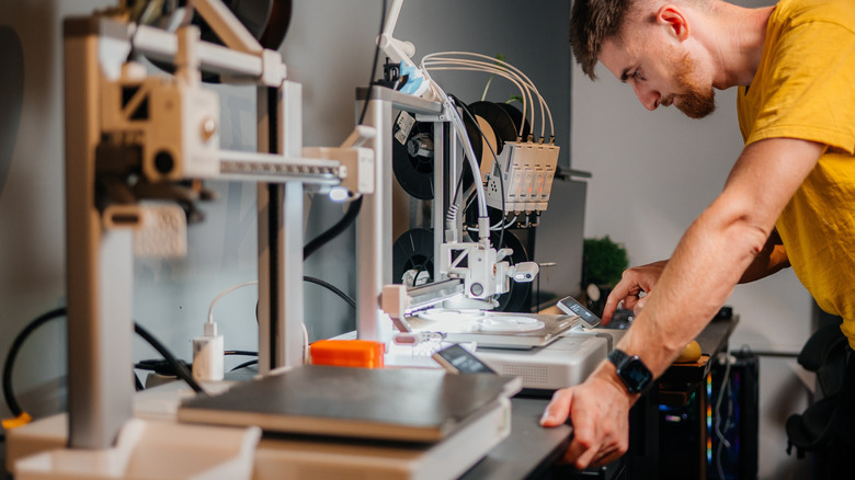 A man getting interacting with the control panel of a 3D printer.