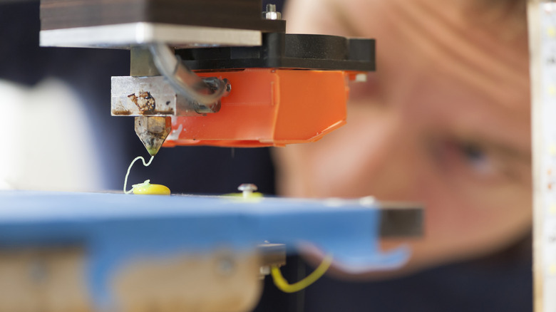 A 3D printer in operation with an observer in the background.