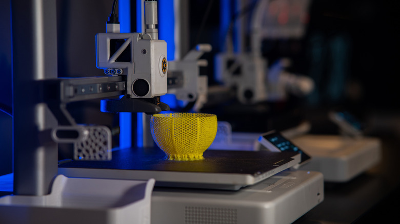 A 3D printer creating a yellow bowl model in a dark environment.