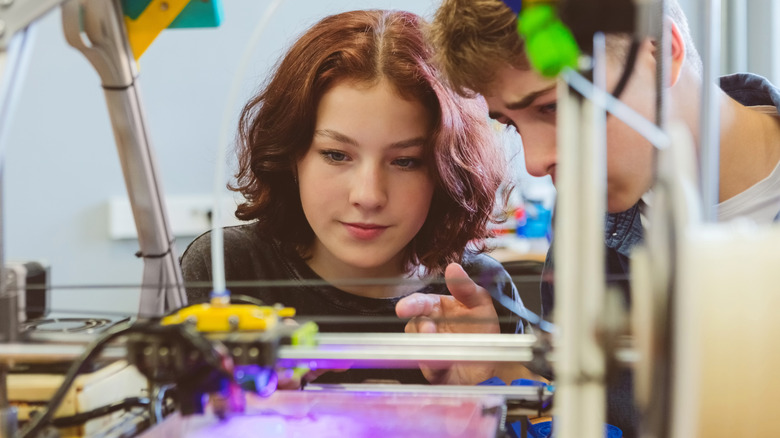 Two people observing a 3D printer in action.