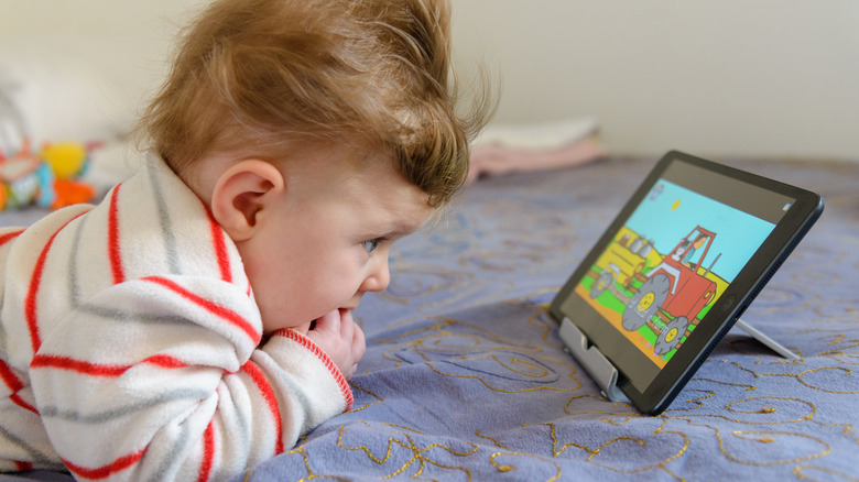 A kid watching a cartoon on a tablet in bed