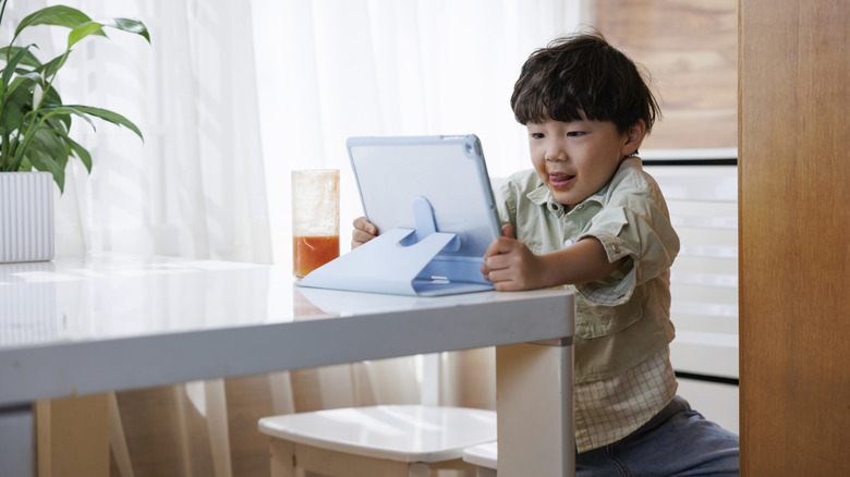 A kid using a tablet at the kitchen table