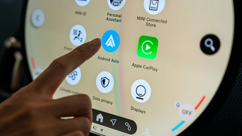 Close up of someone tapping the Android Auto icon on a round in-vehicle display.