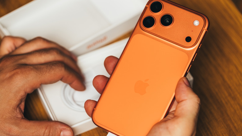 someone holding an iphone 17 pro max in the cosmic orance color