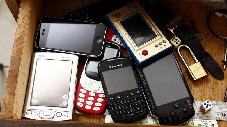 Collection of vintage mobile phones, handheld gadgets, and retro electronics arranged in a drawer.