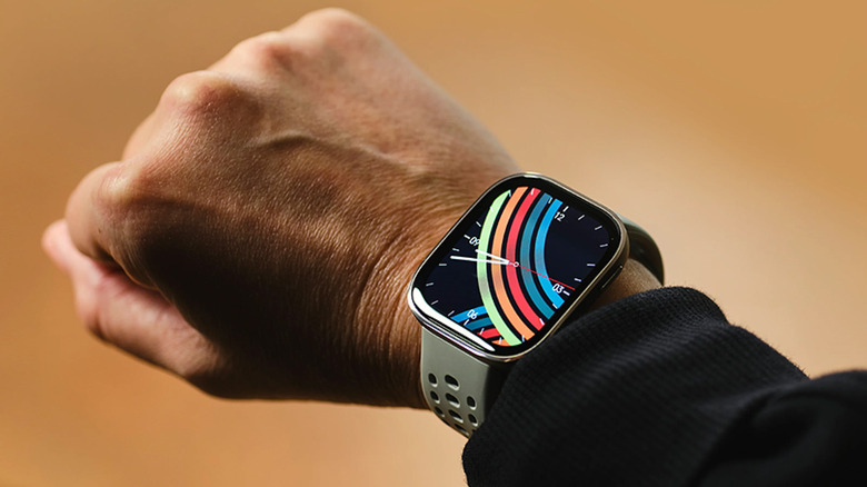 The Amazfit Bip 6 on a man's wrist with an analog clock and colorful background.