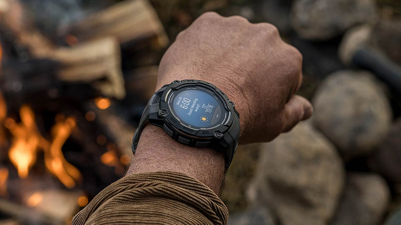 A man's wrist wearing the Garmin Instinct 3 with a campfire in the background.
