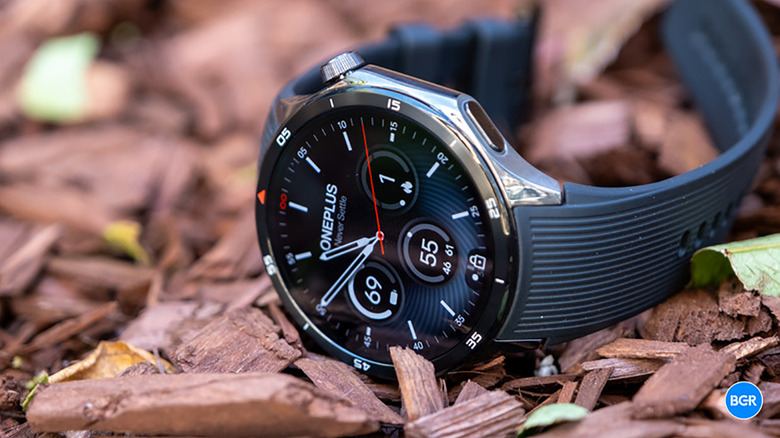 The OnePlus Watch 3 on its side on wood chips outdoors.