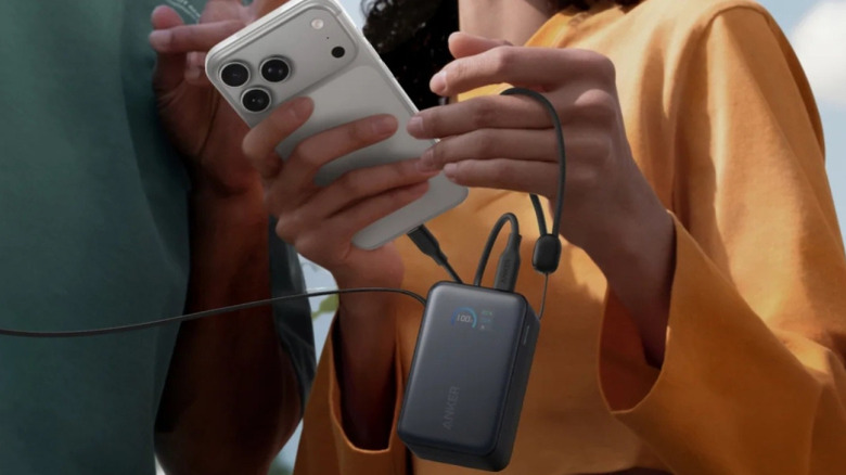 A woman holds a phone that is connected to the Anker A1638 power bank.