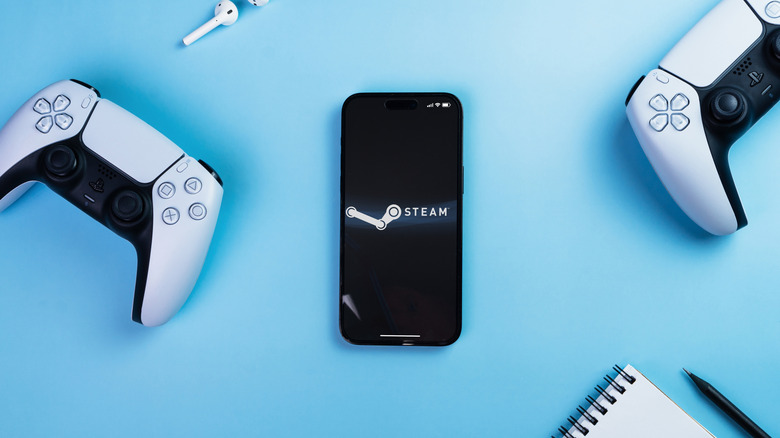 A phone with the Steam logo sits on a blue table surrounded by PS5 controllers