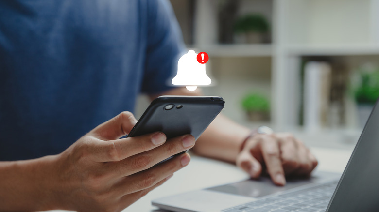person using a smartphone with a notification bell icon above it showing a new notification