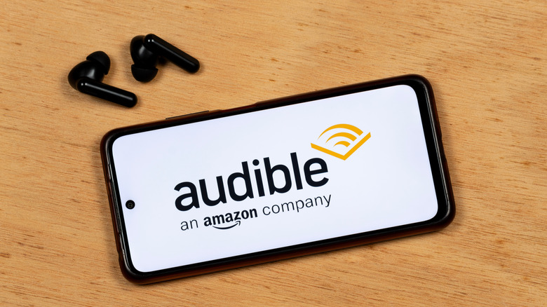 smartphone with audible logo on the screen, earbuds on table beside the phone
