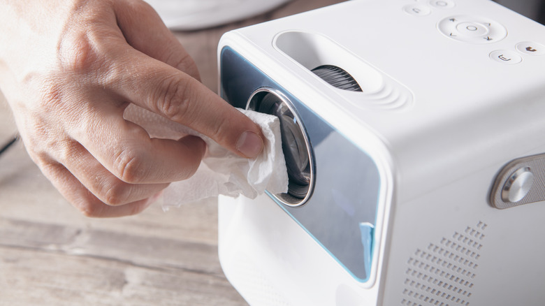 A hand using a cloth to dust off the lens on a home projector