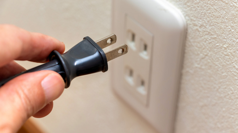 A person removing a power plug from a wall outlet