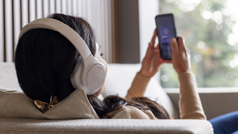 Woman at home listening to music on her phone using headphones while relaxing on the sofa
