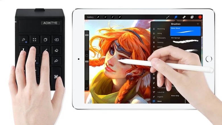 Close up of someone's hands drawing on a tablet and using a stylus in one hand and a Procreate shortcut keyboard in the other.