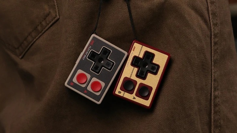 Two small remotes that resemble smaller NES controllers, one gray and red, and the other gold and a darker red