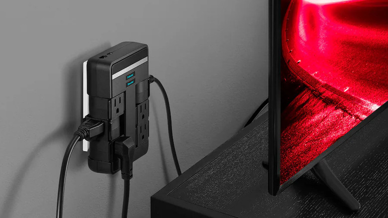A Rocketfish surge protecter plugged into an AC outlet behind a TV.