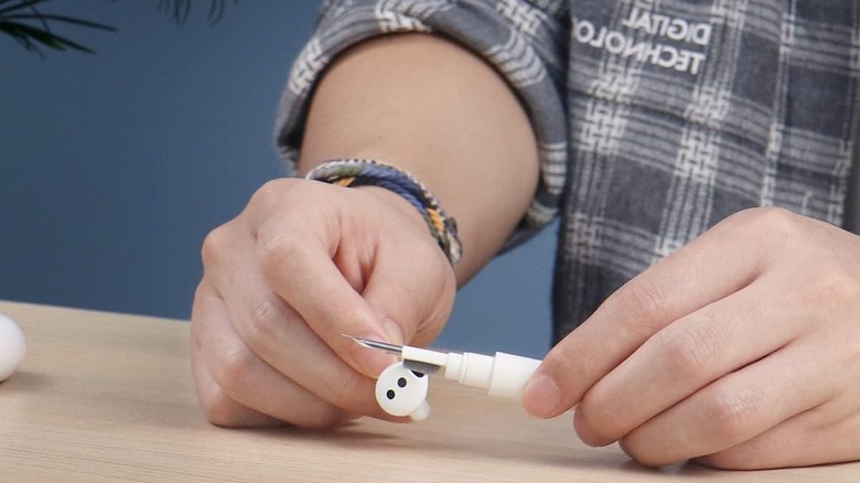 Close up of hands using a cleaning tool to clean a wireless earbud