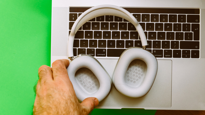 A hand holding a set of AirPods Max against a MacBook keyboard