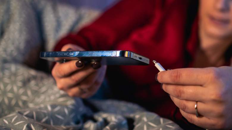 A woman puts her iPhone on charge while she lies in bed