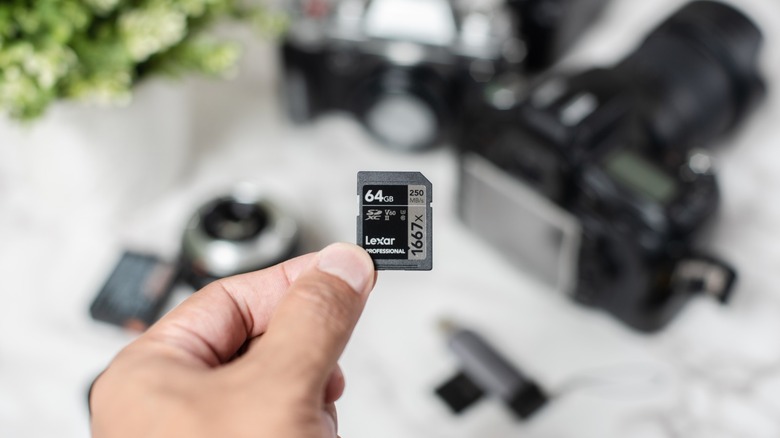 a person holding a 64GB Lexar SD card with camera equipment in the background