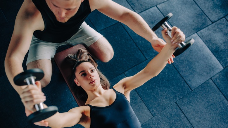 An overhead shot of a man helping a woman with dumbbells.