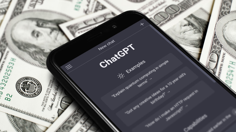 A smartphone laying on top of hundred dollar bills, the phone is displaying a new chat window with ChatGPT